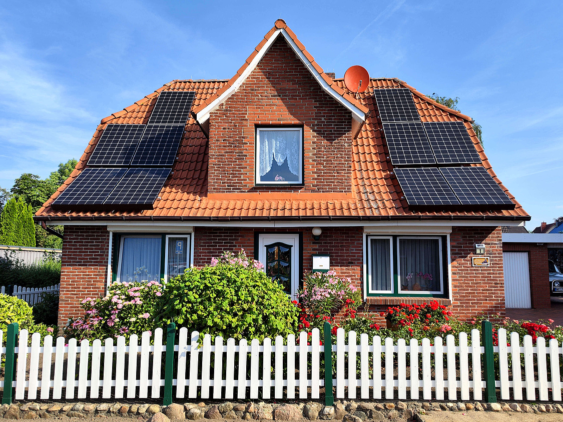 Dieses Foto zeigt ein älteres Haus mit einem hübschen Vorgarten und einer PV-Anlage auf dem Dach
