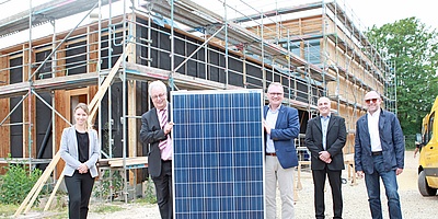 Das Bild zeigt fünf Beteiligte und die Sporthalle mit der Solaranlage (Foto: Stadtwerke Trier)