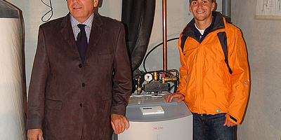 Das Bild zeigt den Biathleten Michael Greis und Dr. Ulrich Stiebel stehend neben der Wärmepumpen-Anlage.