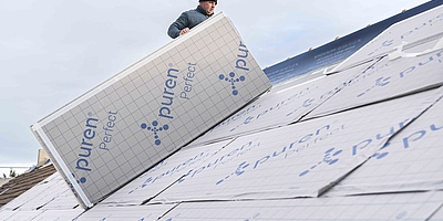 Fachhandwerker verlegt Hartschaumplatte auf der Dachfläche eines Mehrfamilienhauses